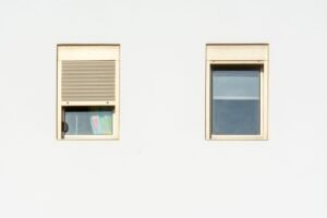Deux fenêtres d'une façade, l'une avec un volet roulant fermé, illustration d'une panne où le volet roulant ne remonte plus