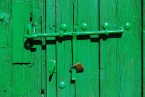 Verrou baïonnette : long verrou à tige coulissante et son cadenas sur une porte en bois peinte en vert