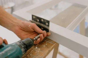 Artisan vissant une paumelle sur un ouvrant à la perceuse