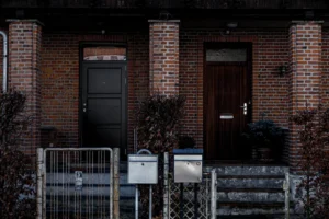 Deux portes d’entrée pleines, l’une noire et l’autre en bois foncé, encastrées dans une façade en brique avec boîtes aux lettres
