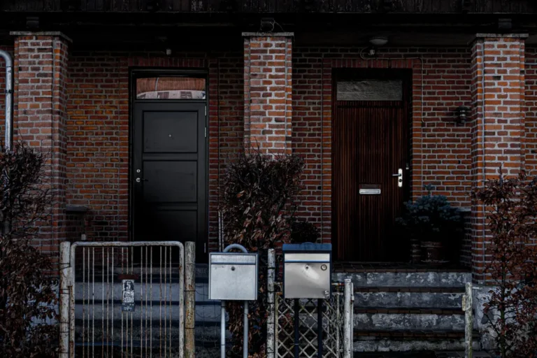 Deux portes d’entrée pleines, l’une noire et l’autre en bois foncé, encastrées dans une façade en brique avec boîtes aux lettres