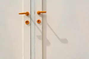 Gros plan sur deux poignées orange et leurs entrées de clé, sur une porte blanche à deux vantaux