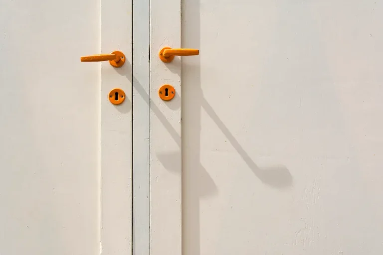 Gros plan sur deux poignées orange et leurs entrées de clé, sur une porte blanche à deux vantaux
