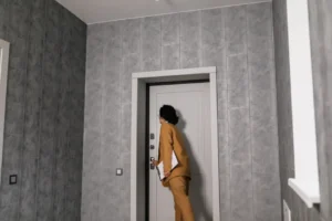 Personne debout dans un couloir face à la porte d’entrée fermée d’un appartement