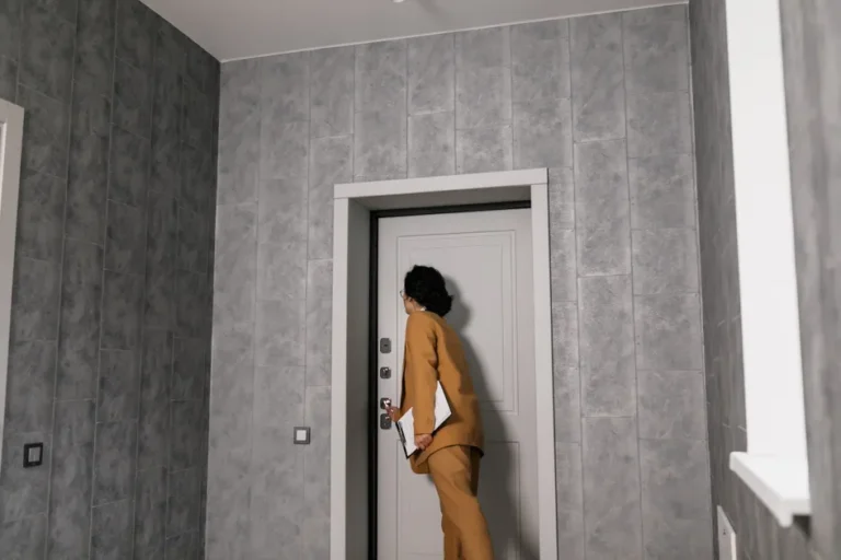 Personne debout dans un couloir face à la porte d’entrée fermée d’un appartement