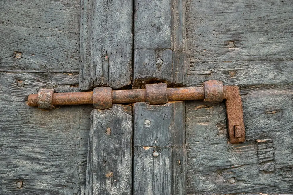 Verrou de porte en applique monté sur un battant en bois : boîtier, pêne cylindrique et pontets de guidage